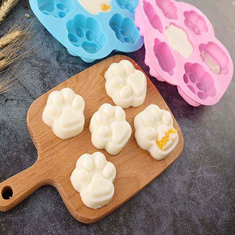 Moules en silicone colorés en forme de pattes et os avec friandises blanches démoulées sur une planche en bois pour pâtisseries et décorations gourmandes.