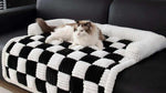 tapis à carreaux noir et blanc doux et rembourré pour chien avec bordure, posé sur canapé avec un chat blanc et beige allongé dessus